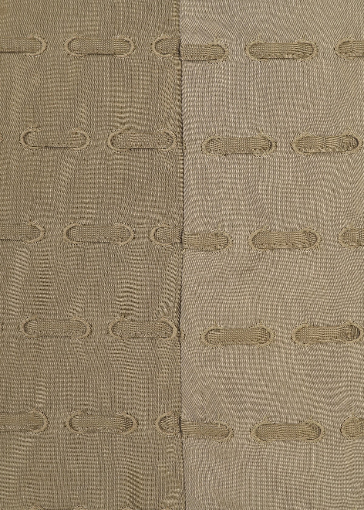 The HOLE & LINE textile by HaaT features two vertical fabric panels—one tan and one light beige—expertly stitched together. Each panel is embellished with rows of oval-shaped cutouts framed by embroidered edges, forming a delicate eyelet embroidery pattern that repeats across the textured surface. view 5 of 8