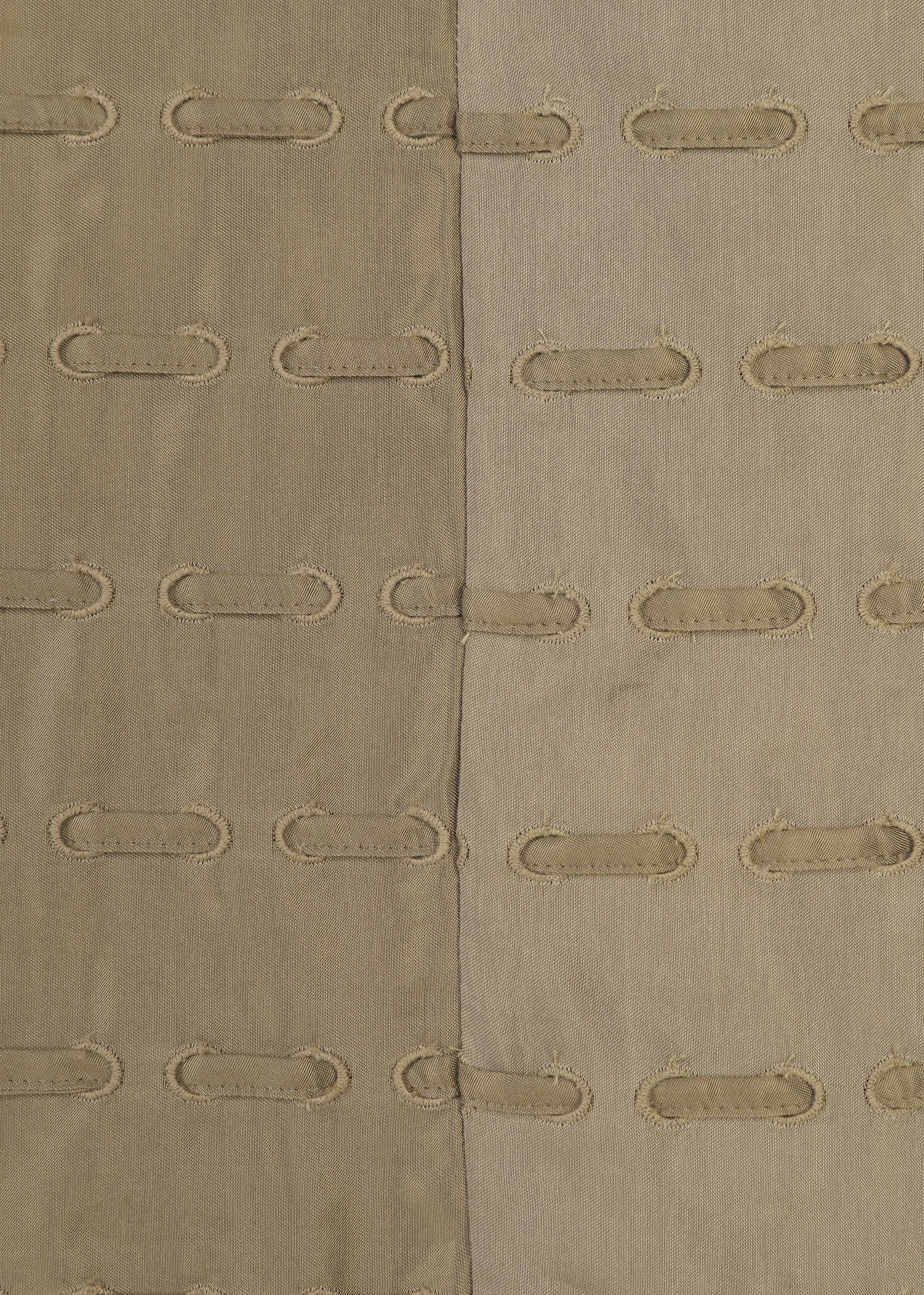 Zoomed view The HOLE & LINE textile by HaaT features two vertical fabric panels—one tan and one light beige—expertly stitched together. Each panel is embellished with rows of oval-shaped cutouts framed by embroidered edges, forming a delicate eyelet embroidery pattern that repeats across the textured surface.