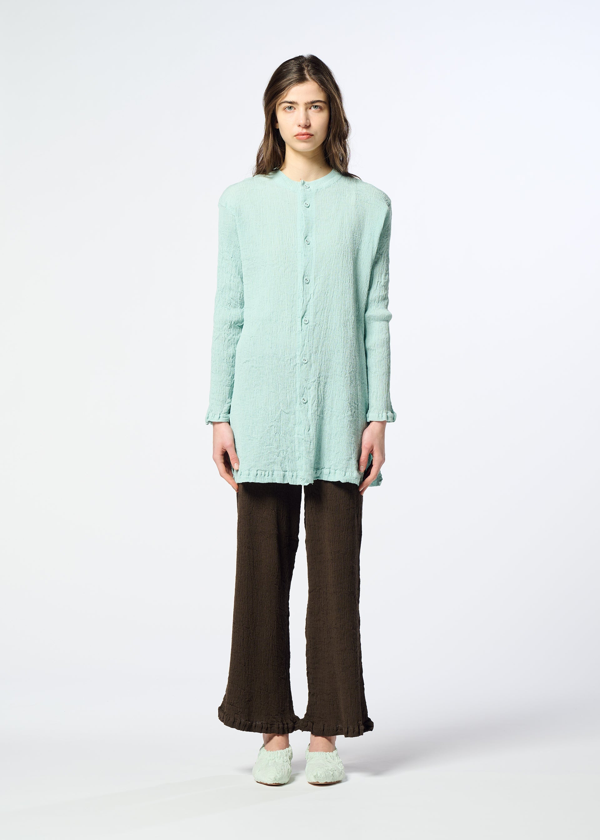 Zoomed view A woman stands facing forward against a plain white background, wearing the HaaT “KYO CHIJIMI AUGUST” light blue long-sleeved cardigan with a subtle crinkled texture, paired with dark brown wide-leg pants and matching light blue shoes.