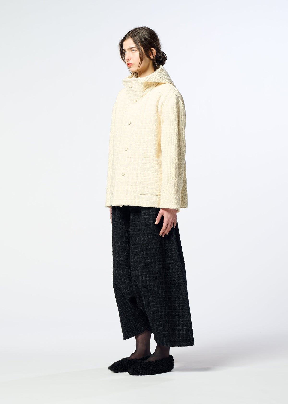 Zoomed view A person stands sideways against a white background, wearing the cream SAKIORI jacket by HaaT, styled with black wide-leg pants and black shoes.