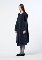 A woman with straight brown hair wears HaaT’s COLLAGE STRETCH Ⅰ—a long, loose-fitting navy blue coat with a subtle large check pattern—paired with a matching skirt, gray tights, and black slip-on shoes, standing against a plain white background.