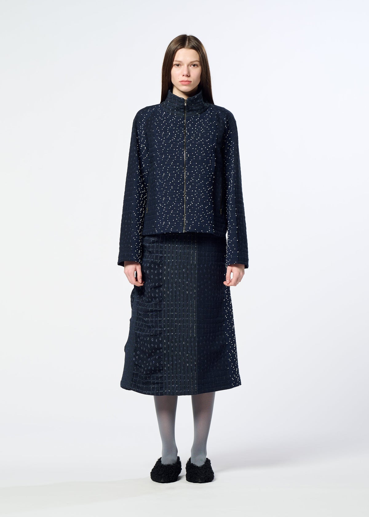 A woman stands facing forward against a plain white background, wearing HaaT’s COLLAGE STRETCH Ⅰ navy blue jacquard-patterned jacket and matching midi skirt, paired with gray tights and black shoes. view 6 of 8