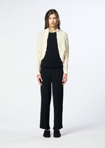 A person stands against a plain background, wearing the cream-colored KYO CHIJIMI 2WAY jacket from HaaT, featuring a subtle crinkle texture. The jacket is layered over a black top and black pants, paired with black shoes. The individual faces forward with arms relaxed at their sides.