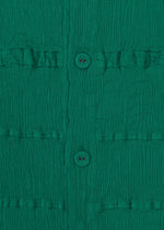 Close-up of KYO CHIJIMI TSUCHIKABE by HaaT: ultra-fine cotton green fabric with a crepe texture, vertical row of two buttons, and subtle grid pattern formed by horizontal stitched lines.