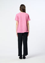 A person stands facing away, wearing the HaaT KYO CHIJIMI 2WAY pink short-sleeved tunic, paired with black pants and black shoes against a plain white background.