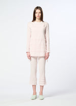 A young woman with straight brown hair stands facing forward, wearing HaaT’s KYO CHIJIMI TSUCHIKABE pale pink ultra-fine cotton tunic and matching cropped pants with ruffle details, plus light green slippers, against a plain white background.