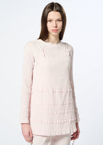 A young woman with straight brown hair wears HaaT’s KYO CHIJIMI TSUCHIKABE light pink apron-style top and matching pants with textured stripes and a crepe-like cotton feel, standing against a plain white background.