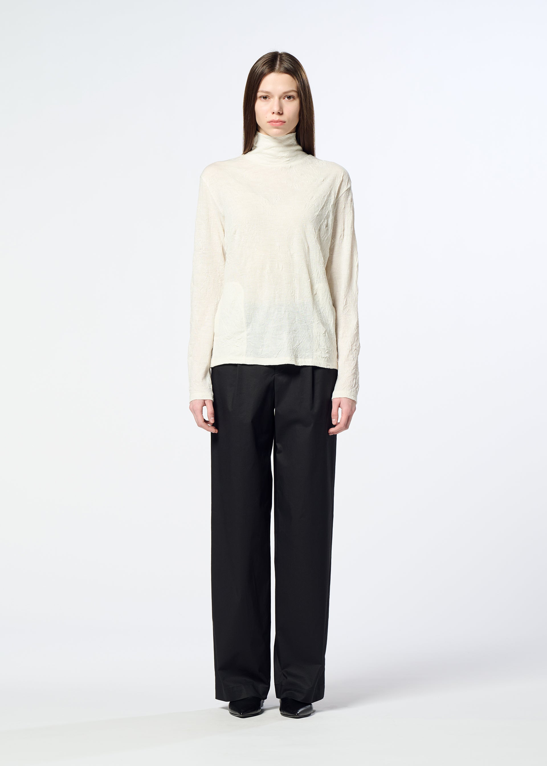 Zoomed view A person stands facing forward against a plain white background, wearing HaaT’s W/P WASHER cream wool jersey turtleneck sweater and loose black trousers.