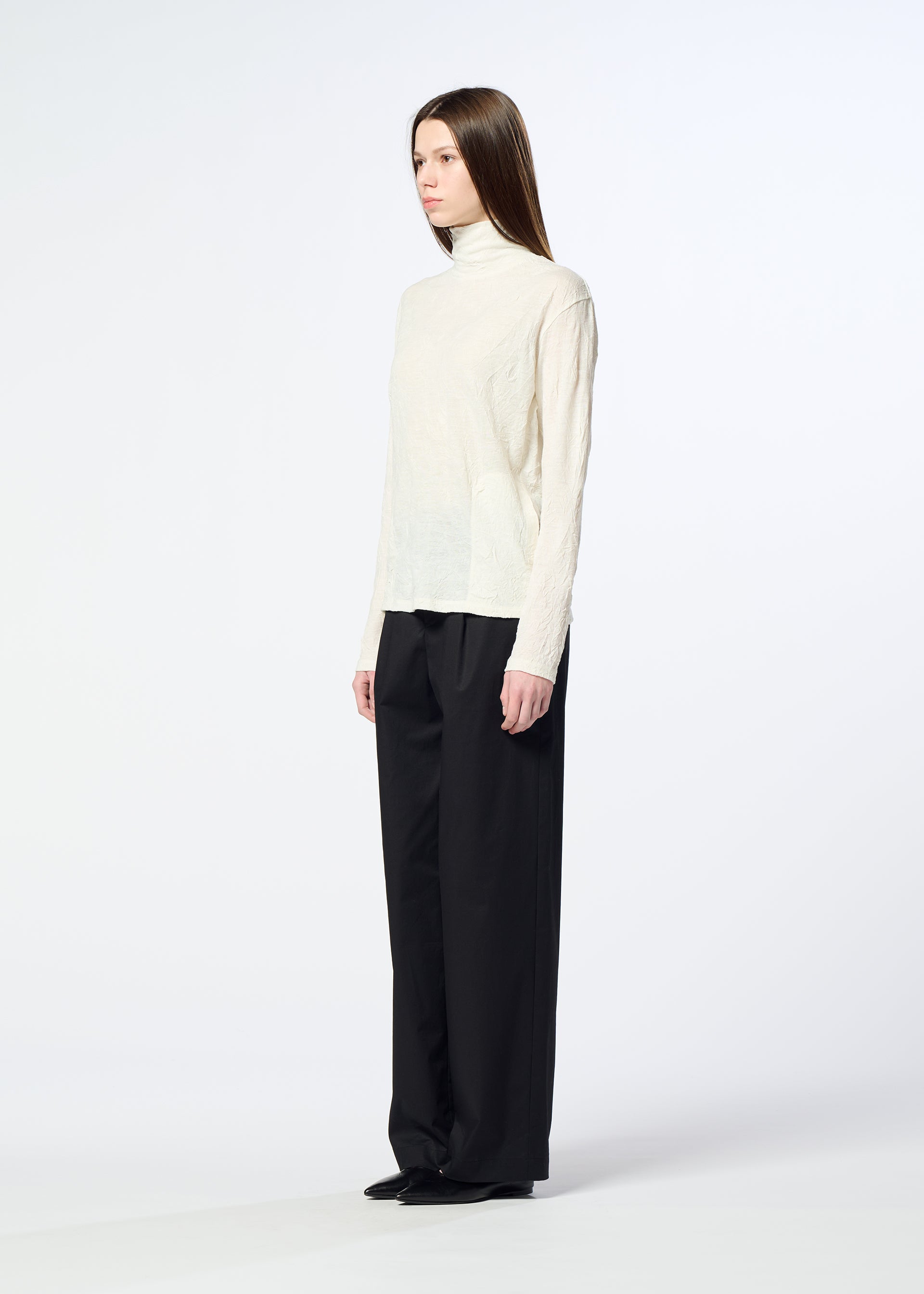 Zoomed view A person stands sideways against a plain white background, wearing the HaaT W/P WASHER cream wool jersey turtleneck sweater, loose black trousers, and black shoes.