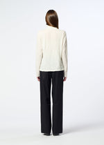 A person with long hair, seen from behind, is wearing HaaT’s W/P WASHER cream-colored high-neck wool jersey top and loose black trousers, standing against a plain white background.