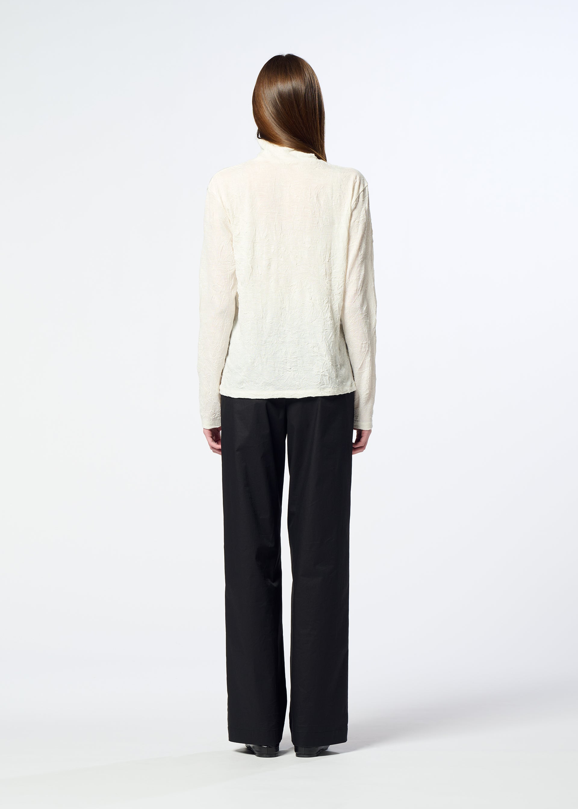 Zoomed view A person with long hair, seen from behind, is wearing HaaT’s W/P WASHER cream-colored high-neck wool jersey top and loose black trousers, standing against a plain white background.