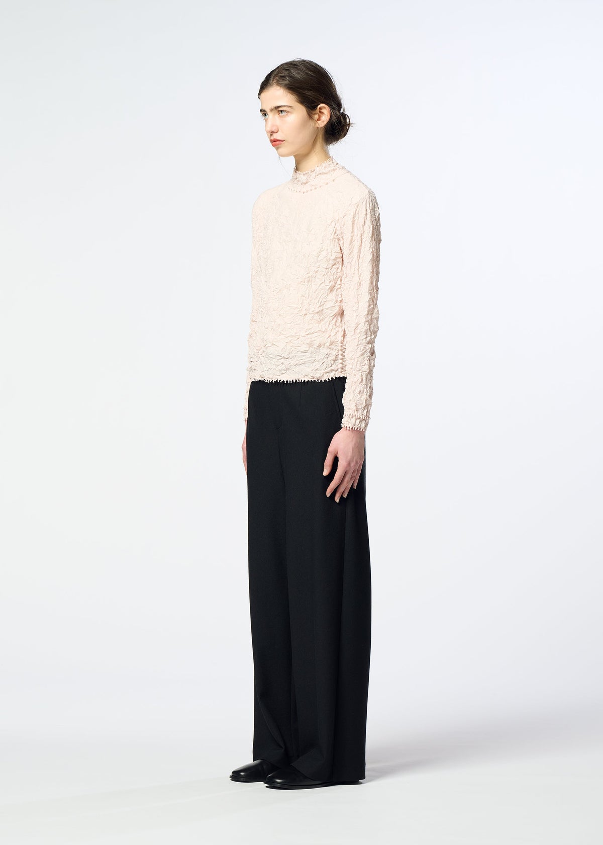 A person stands sideways wearing the HaaT KUMO SHIBORI textured long-sleeve tricot jersey top with loose black pants and black shoes, set against a plain white background. view 9 of 10