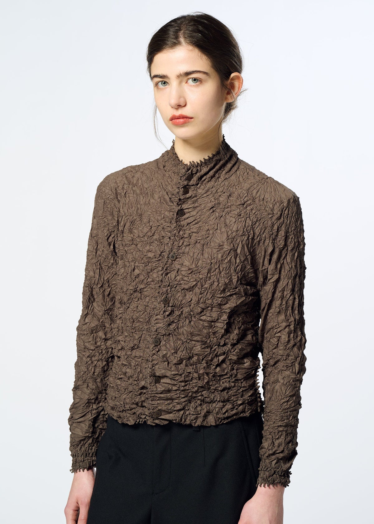 Zoomed view A person with long dark hair in a low bun wears the HaaT KUMO SHIBORI textured, brown crinkled long-sleeve shirt with black pants against a plain light background.