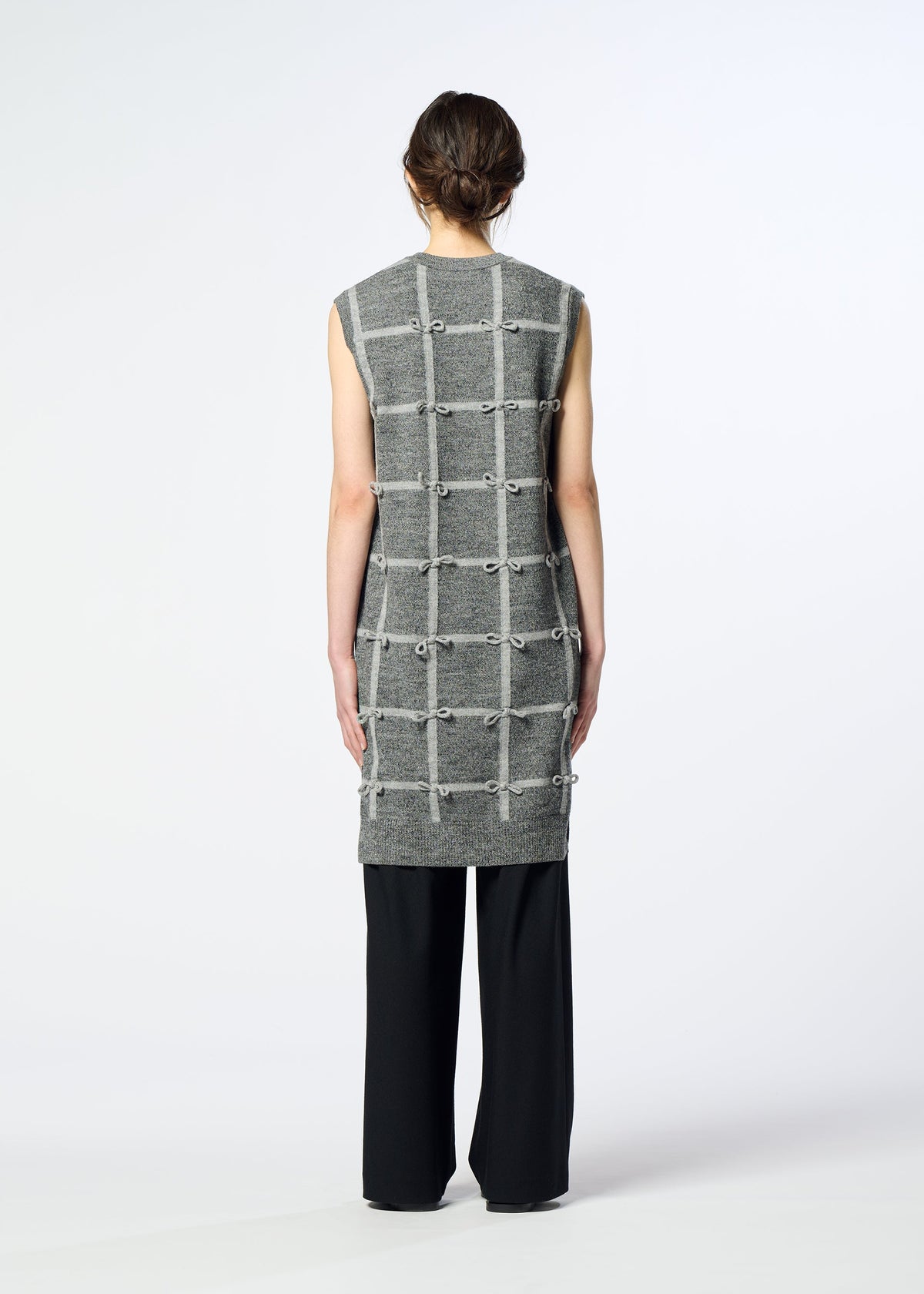 Zoomed view A person faces away, wearing the HaaT RIBBON KNIT sleeveless grey tunic with a grid pattern, paired with black pants against a plain white background.