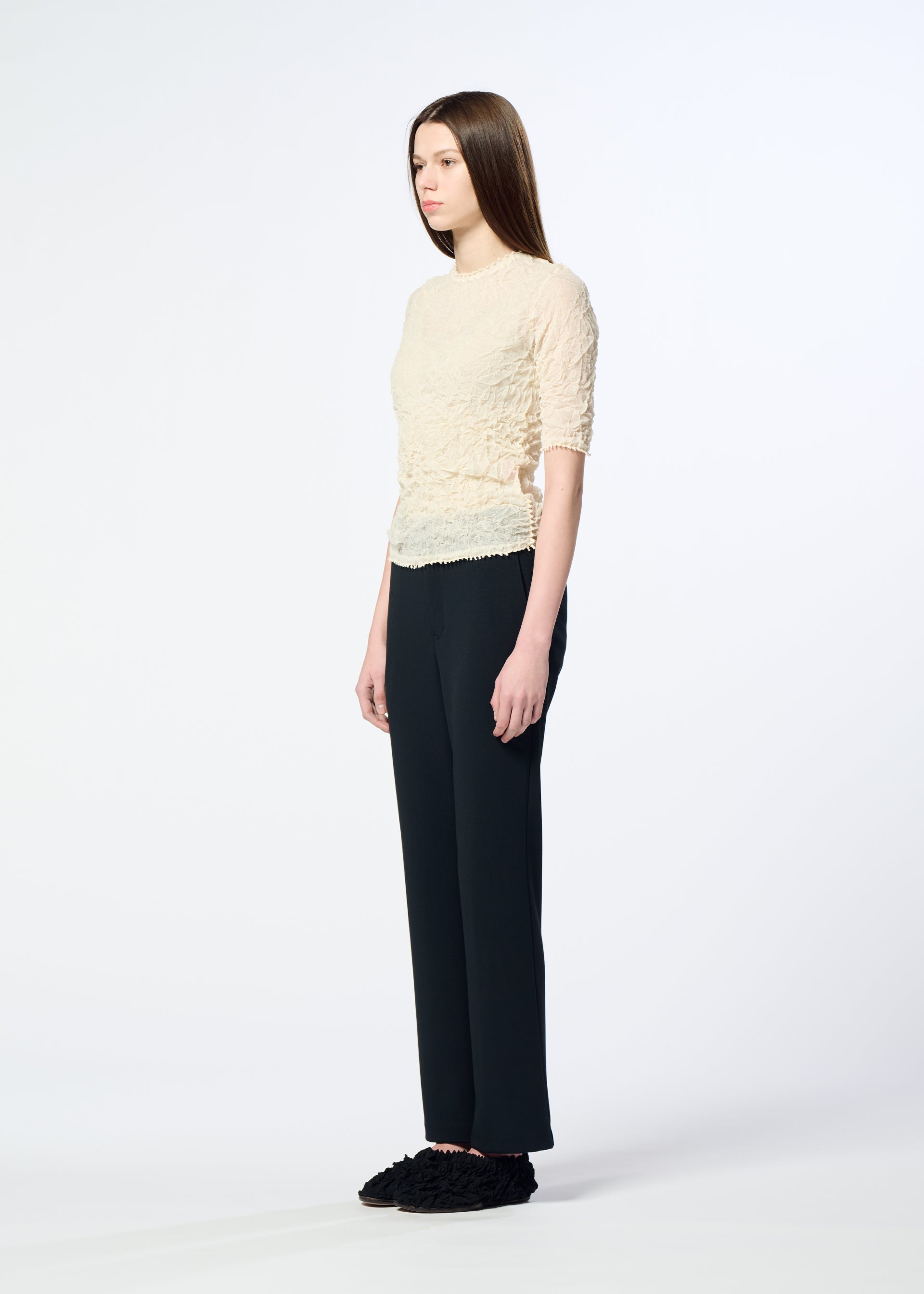 Zoomed view A person with long straight hair stands sideways against a plain light background, wearing the HaaT KUMO SHIBORI KNIT SHEER top, loose black pants, and black fuzzy slippers.