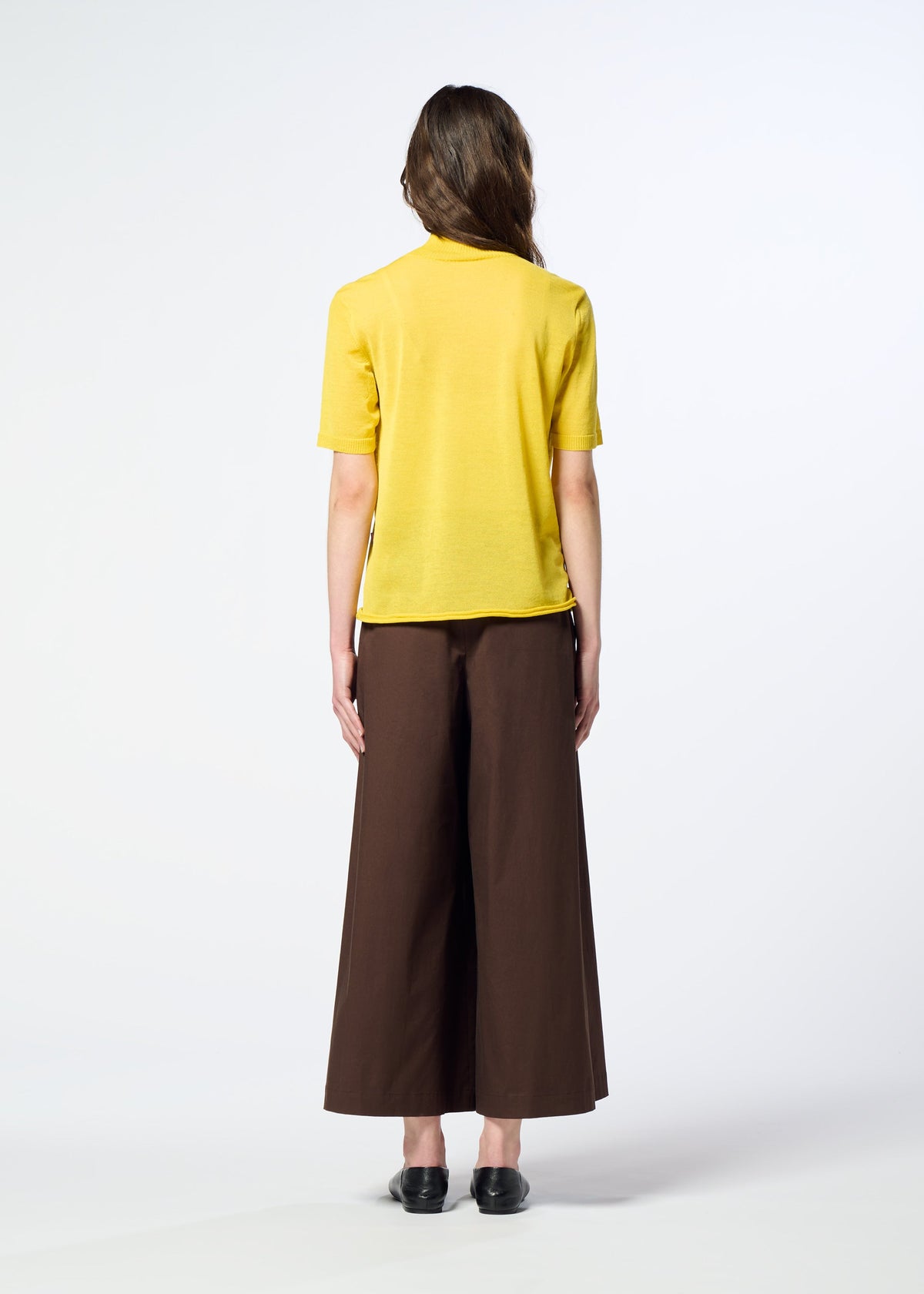 A person stands facing away, dressed in HaaT’s AIRY POCKET LAYERS—a short-sleeved knit yellow shirt—paired with wide-legged brown pants made from a polyester wool blend and black shoes, set against a plain, light background. view 8 of 8