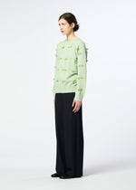 A person stands sideways in the HaaT RIBBON KNIT, a light green long-sleeved sweater with small knots, paired with loose black wide-leg pants against a plain white background.
