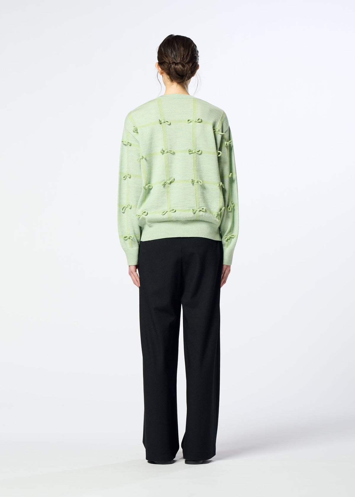 A person faces away, wearing the HaaT RIBBON KNIT in light green with tied ribbons and loose black trousers, set against a plain light background. view 7 of 7