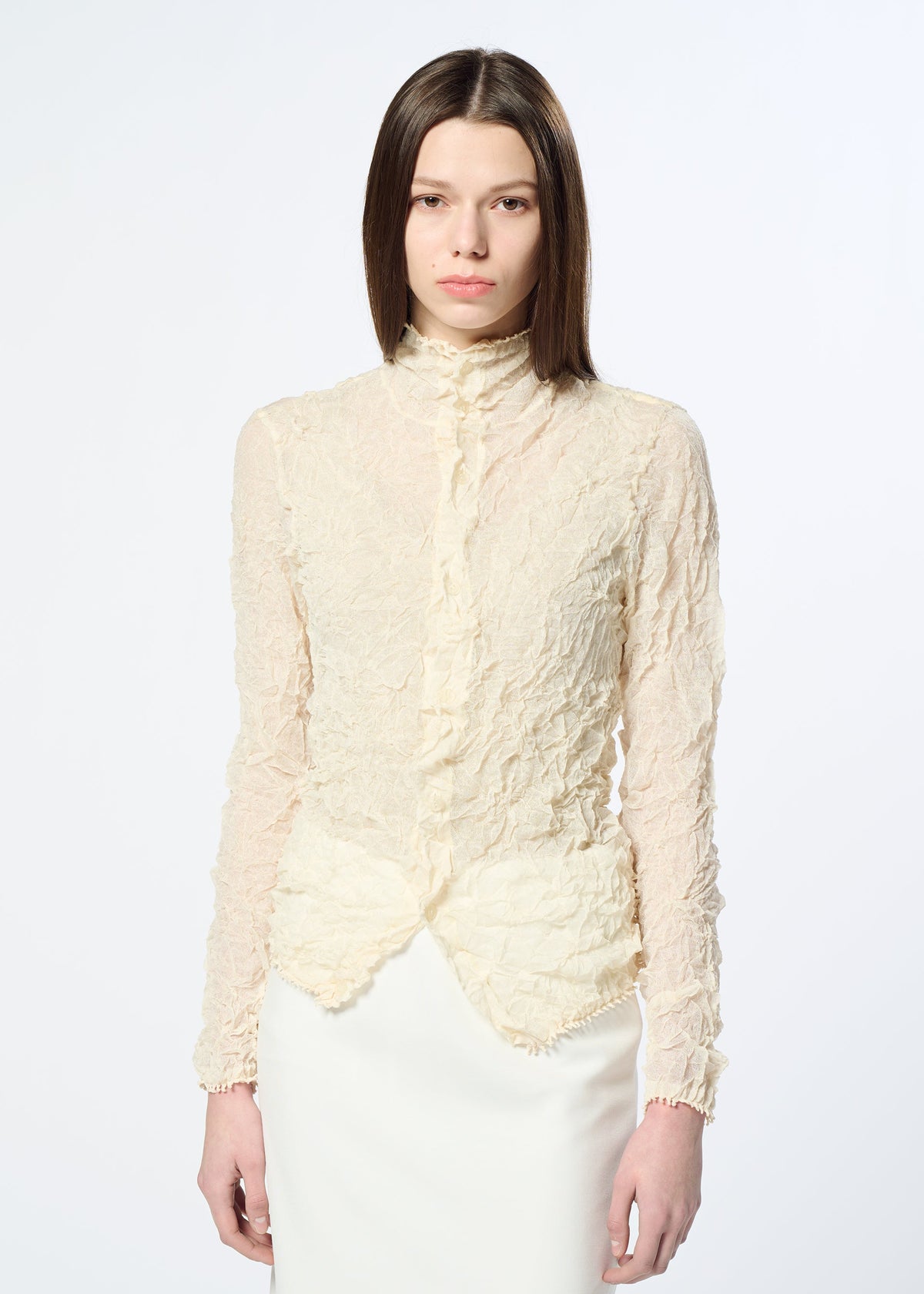 A person with straight brown hair wears HaaT's KUMO SHIBORI KNIT SHEER, a high-neck, long-sleeve, textured cream ramie-blend blouse and matching skirt, standing against a plain white background. view 9 of 9