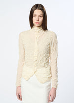 A person with straight brown hair wears HaaT's KUMO SHIBORI KNIT SHEER, a high-neck, long-sleeve, textured cream ramie-blend blouse and matching skirt, standing against a plain white background.