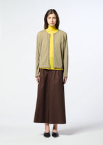 A woman stands against a plain background, wearing HaaT’s AIRY POCKET LAYERS – a beige long-sleeved cardigan crafted from a soft polyester wool blend. She pairs it with a yellow turtleneck, a brown ankle-length skirt, and black flats, facing forward with a neutral expression.