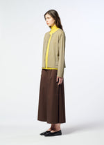 A woman stands sideways against a plain white background, wearing HaaT’s AIRY POCKET LAYERS—a long-sleeved beige cardigan crafted from a polyester wool blend—paired with a yellow turtleneck, a long brown skirt, and black shoes.