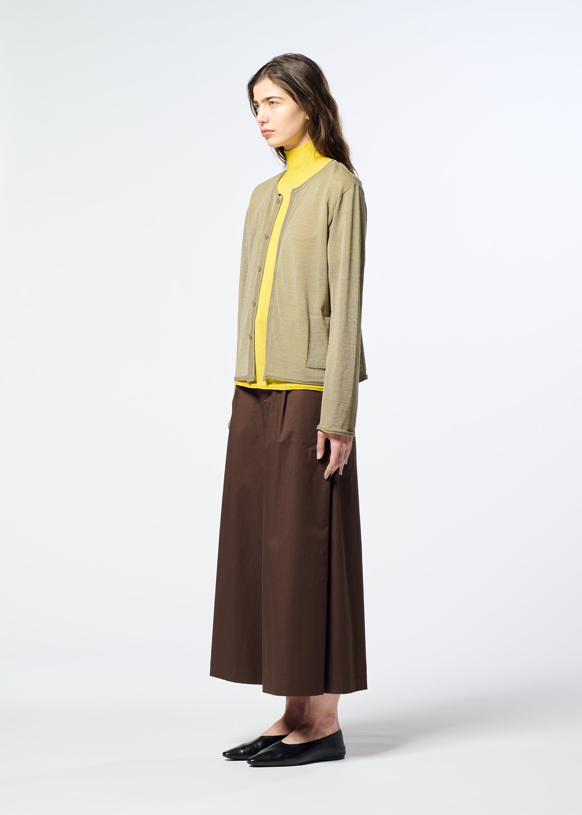 Zoomed view A woman stands sideways against a plain white background, wearing HaaT’s AIRY POCKET LAYERS—a long-sleeved beige cardigan crafted from a polyester wool blend—paired with a yellow turtleneck, a long brown skirt, and black shoes.