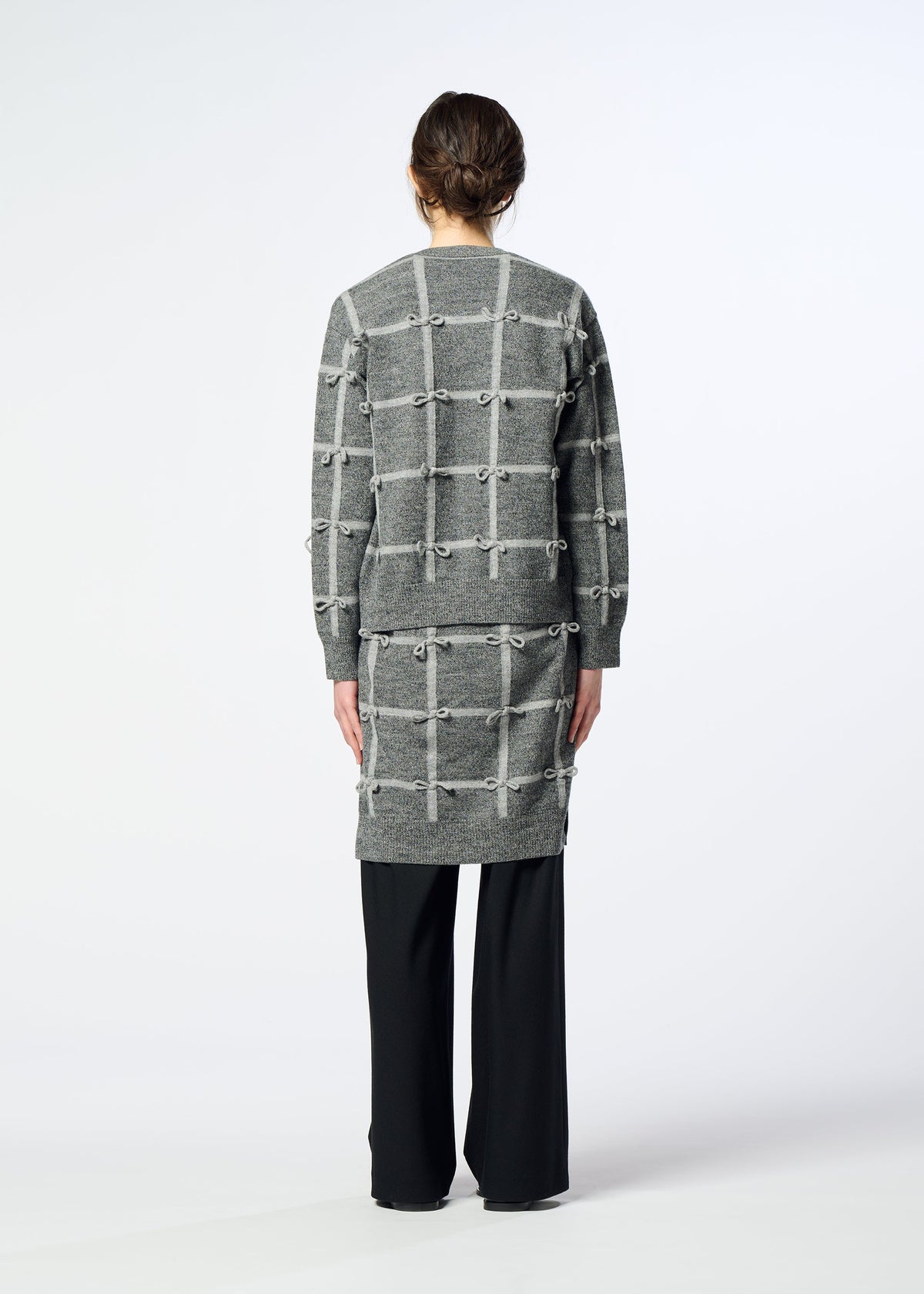 A person stands facing away, wearing the HaaT RIBBON KNIT long-sleeved cardigan with a grid pattern over black pants, against a plain light background. view 7 of 7