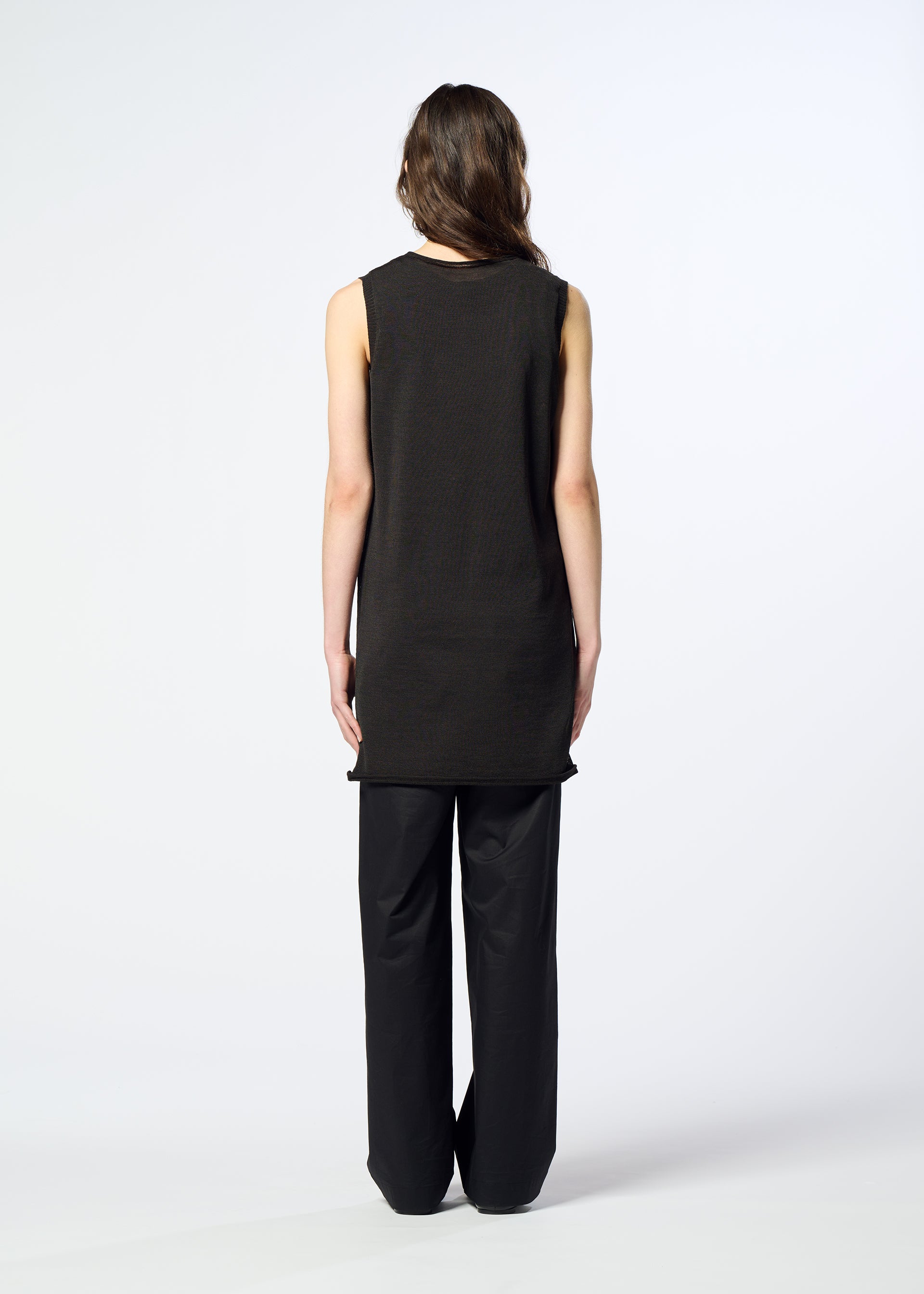 Zoomed view A person with long hair stands facing away from the camera, wearing HaaT’s AIRY POCKET LAYERS—a sleeveless black tunic layered over loose black pants—against a plain white background.