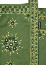 The DAZZLE MIRROR BOX by HaaT is a green fabric mini tote bag adorned with yellow and dark green Bhill embroidery patterns, mirror accents, and a decorative handle. Lovingly crafted by Indian artisans, it features a black label with white HaaT branding attached to the bag.