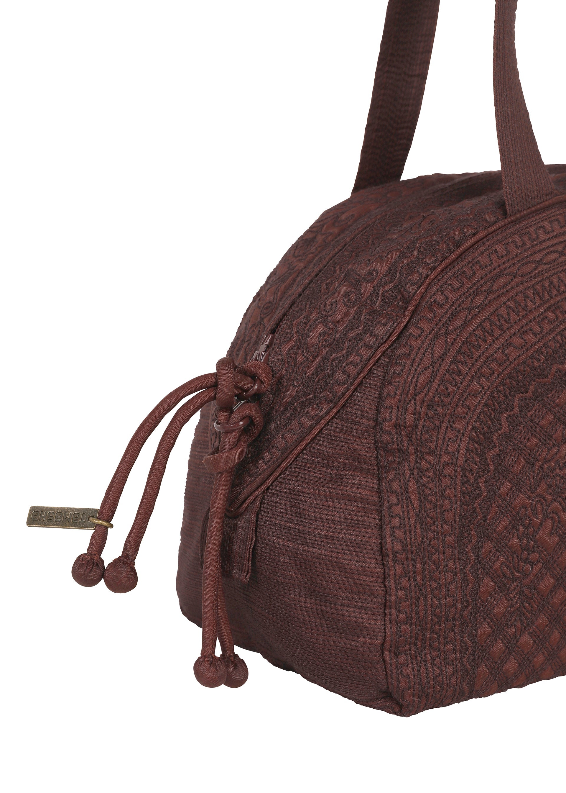 Zoomed view Close-up of the HaaT BLOOM & PLAID BOSTON bag in brown fabric, adorned with intricate Bhill embroidery that highlights the craftsmanship of Indian artisans. The bag includes a zipper closure with two knotted pulls and is accented by a small rectangular metallic tag hanging from the zipper.