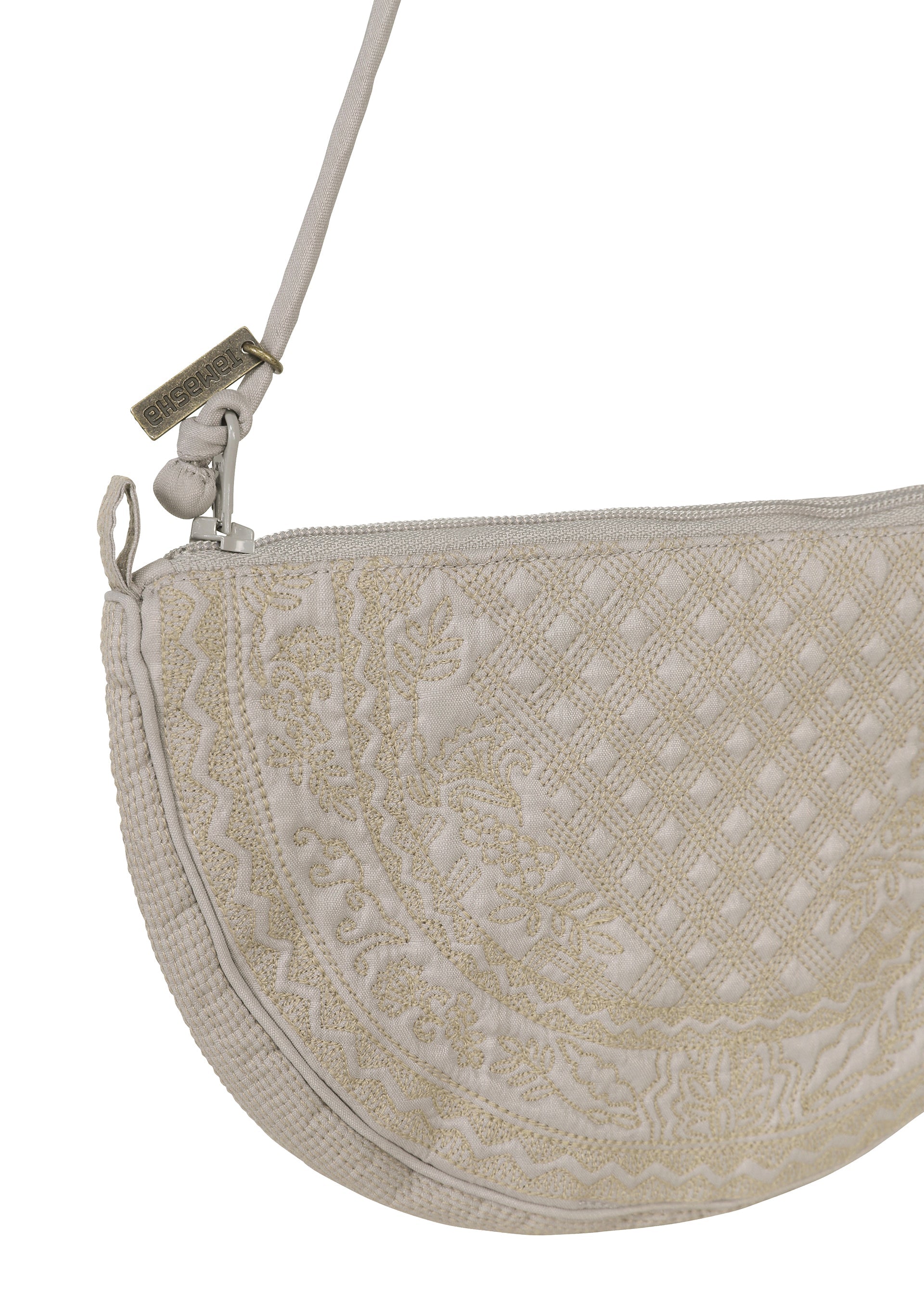 Zoomed view Introducing the BLOOM & PLAID BOSTON by HaaT—a cream-colored, half-moon crossbody bag featuring intricate Bhill embroidery, a zipper closure, and a slim strap adorned with a small metal tag. Expertly crafted in India, this elegant pouch blends timeless style with artisanal craftsmanship.