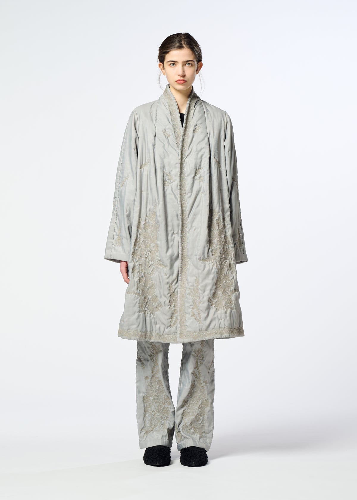 A person faces forward, wearing the DELICATE FLORAL BHILL by HaaT—a loose, light gray evening coat with botanical embroidery and matching pants—paired with black shoes against a plain white background. view 7 of 9