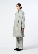 A person stands sideways wearing the DELICATE FLORAL BHILL by HaaT, a light gray oversized quilted coat with subtle botanical patterns and matching pants, paired with dark slippers against a plain white background.