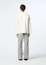 A person with dark hair in a low bun faces away, wearing a textured white sweater and HaaT DELICATE FLORAL BHILL loose, light gray nylon pants with a subtle botanical pattern against a plain background.