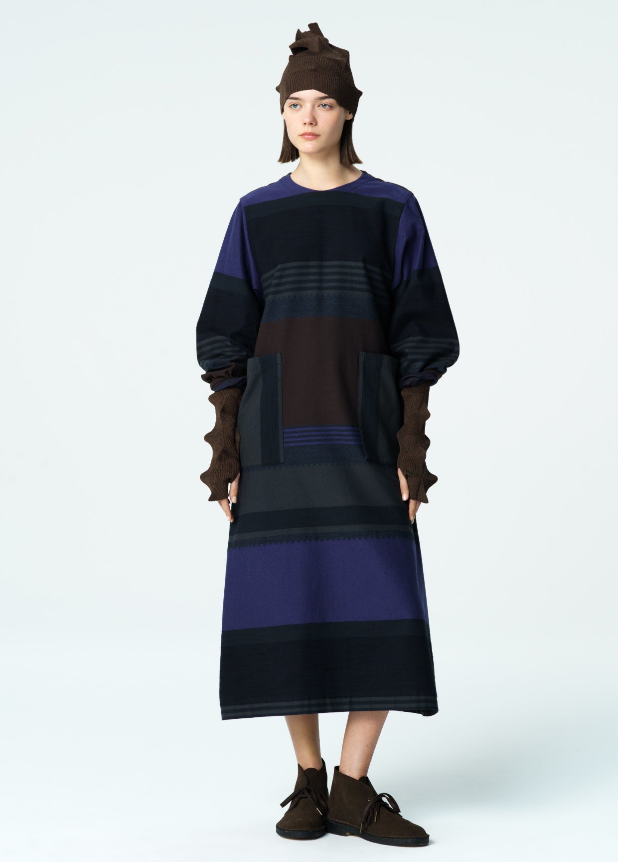 Person wearing a long, dark blue and brown striped dress with a matching hat on a white background