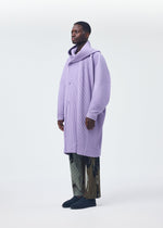 A person wears the oversized lilac textured "MONTHLY COLORS : DECEMBER" coat by HOMME PLISSÉ ISSEY MIYAKE, styled with patterned trousers and black shoes, standing against a plain light background and looking slightly left.