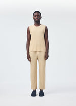A person with short hair wears the TAILORED PLEATS 2 sleeveless beige set from HOMME PLISSÉ ISSEY MIYAKE—featuring a round-neck vest and ribbed quick-drying polyester pants—with dark slip-on shoes against a plain white background.