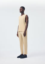 A person stands against a white background wearing the HOMME PLISSÉ ISSEY MIYAKE TAILORED PLEATS 2 beige round-neck vest and matching pants in ribbed quick-drying polyester, paired with dark slip-on shoes.