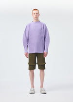 A person with short red hair faces forward in a loose light purple ribbed sweater, olive green HOMME PLISSÉ ISSEY MIYAKE PLEATS BOTTOMS 2 shorts with pockets and panels, and light gray slip-on shoes against a plain white background.