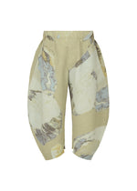 The PAINTED STONE pants by HOMME PLISSÉ ISSEY MIYAKE are beige cropped trousers with an abstract marble-like pattern in gray, white, and yellow tones, featuring wide rounded legs and textured fabric.