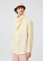 A person in a light yellow button-up shirt, pale pink pleated pants, and the HOMME PLISSÉ ISSEY MIYAKE CROCHET HAT stands against a plain light background, gazing slightly to the side.