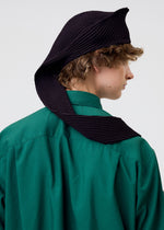 A person with curly hair wears a green collared shirt and the HOMME PLISSÉ ISSEY MIYAKE PLEATED SEERSUCKER TIE, styled uniquely to drape over their shoulder, photographed from behind against a plain background.