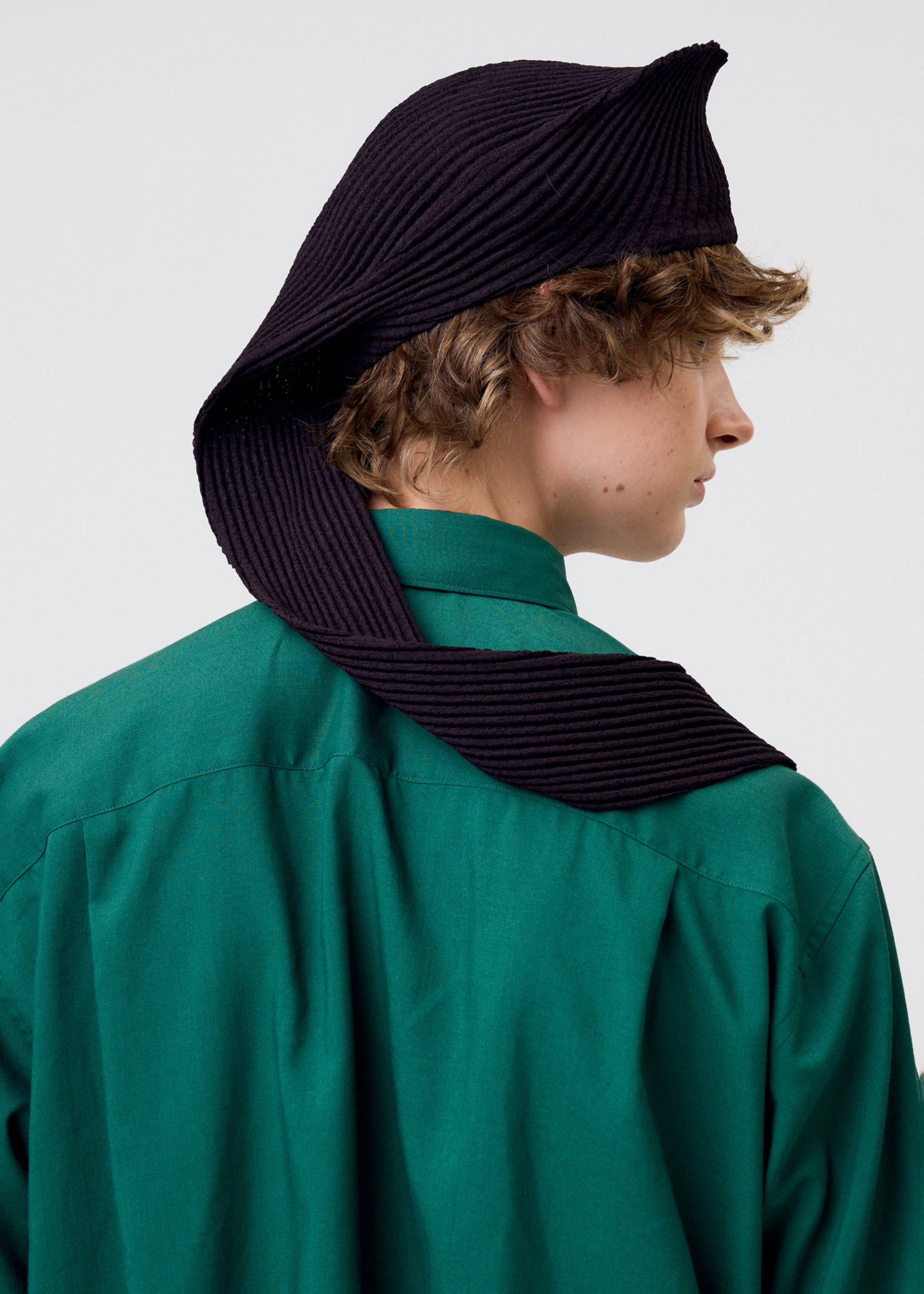 Zoomed view A person with curly hair wears a green collared shirt and the HOMME PLISSÉ ISSEY MIYAKE PLEATED SEERSUCKER TIE, styled uniquely to drape over their shoulder, photographed from behind against a plain background.