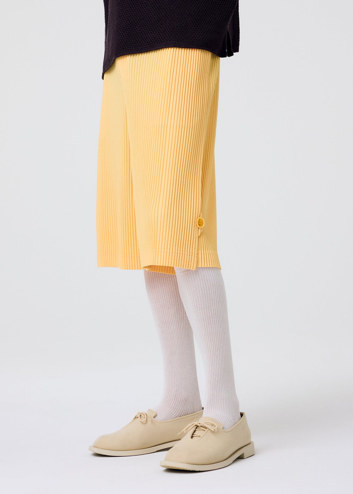A person wearing yellow pleated knee-length shorts, beige shoes, a dark top, and HOMME PLISSÉ ISSEY MIYAKE WASHI BLEND SOCKS stands against a plain white background. view 7 of 7