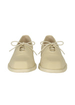 CIOCCOLATO by HOMME PLISSÉ ISSEY MIYAKE: beige minimalist lace-up shoes with an oblique toe, shown front-facing on a white background, capturing the brand’s refined aesthetic.