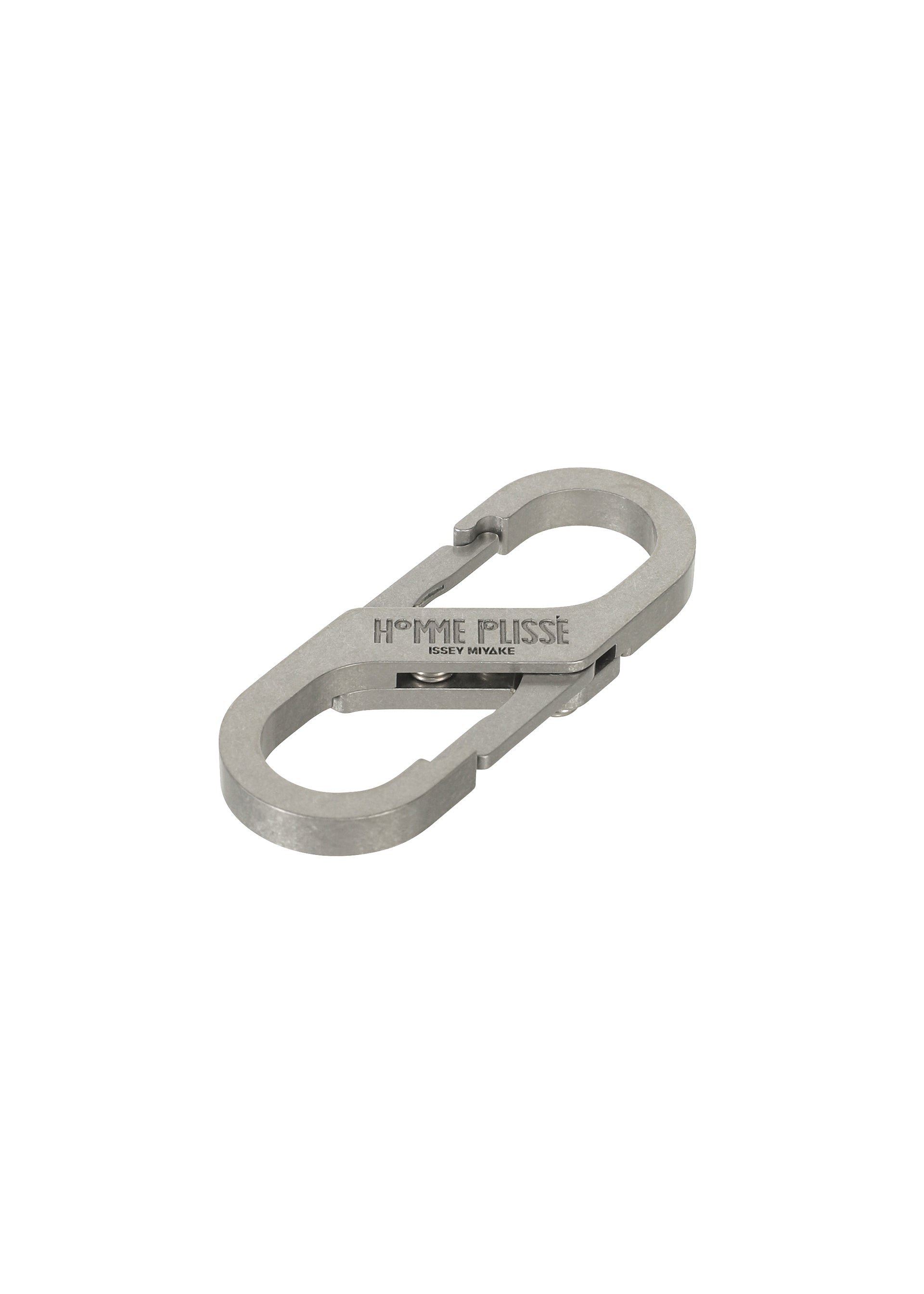 Zoomed view The CARABINER by HOMME PLISSÉ ISSEY MIYAKE is a silver metal keychain shaped like two connected carabiners, engraved with the brand name and shown against a white background, perfect as a sleek belt loop accessory.