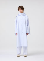 A person with short curly hair wears the FRESHEN hooded coat and matching wide-legged pants by HOMME PLISSÉ ISSEY MIYAKE, styled with beige shoes against a plain background.