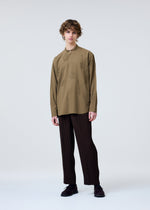 A person with curly hair wears the HOMME PLISSÉ ISSEY MIYAKE EMBROIDERY PRESS SHIRT in olive green and loose black pinstriped trousers, standing against a plain light grey background.
