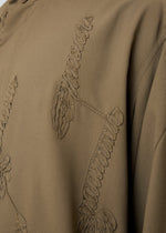 Close-up of the EMBROIDERY PRESS SHIRT by HOMME PLISSÉ ISSEY MIYAKE, featuring khaki fabric adorned with raised, textured embroidery in abstract, organic-inspired patterns.